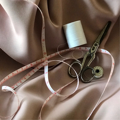 fabric scissors, a spool of thread, and a measuring tape on a silk fabrics