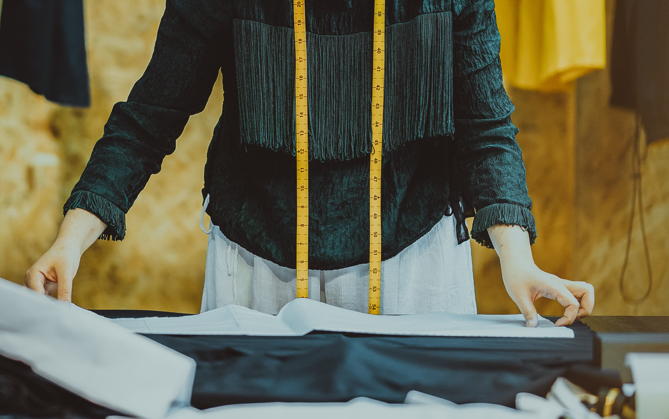 a person with a measuing tape around their neck lining up a fabric pattern on to a black fabric 